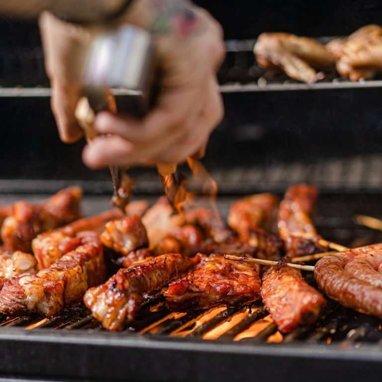 Gegrilltes Fleisch auf einem Grill, mit einer Hand, die Gewürze darüber streut.